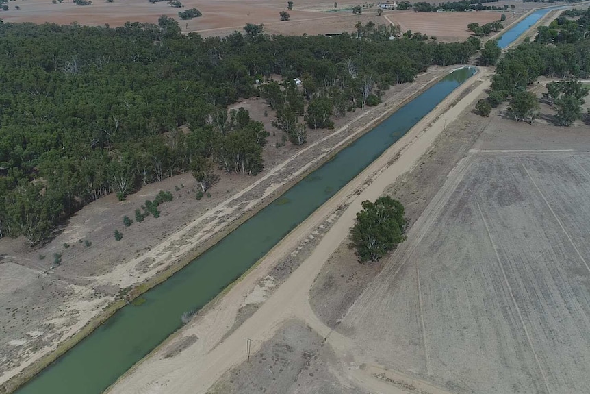 A skinny canal of water stretches diagonally across the image, with green gumtrees on the far side & bare paddocks on the other