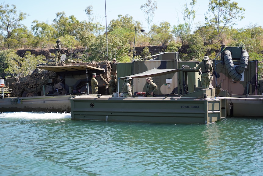 A wide shot of soldiers on board a camouflaged floating command post. 