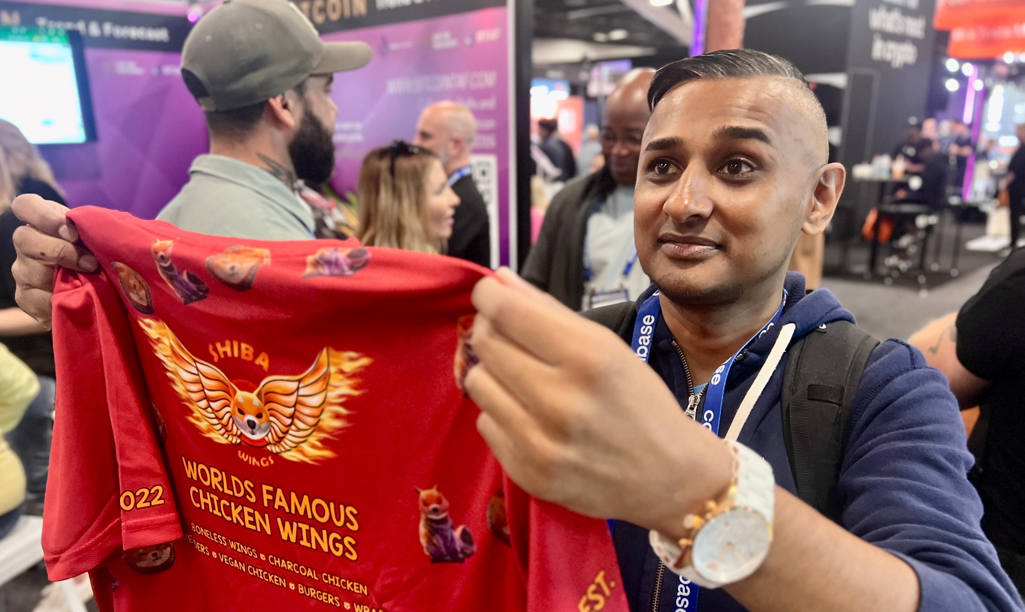 Man holds red t-shirt up to camera that says 'worlds famous chicken wings'.