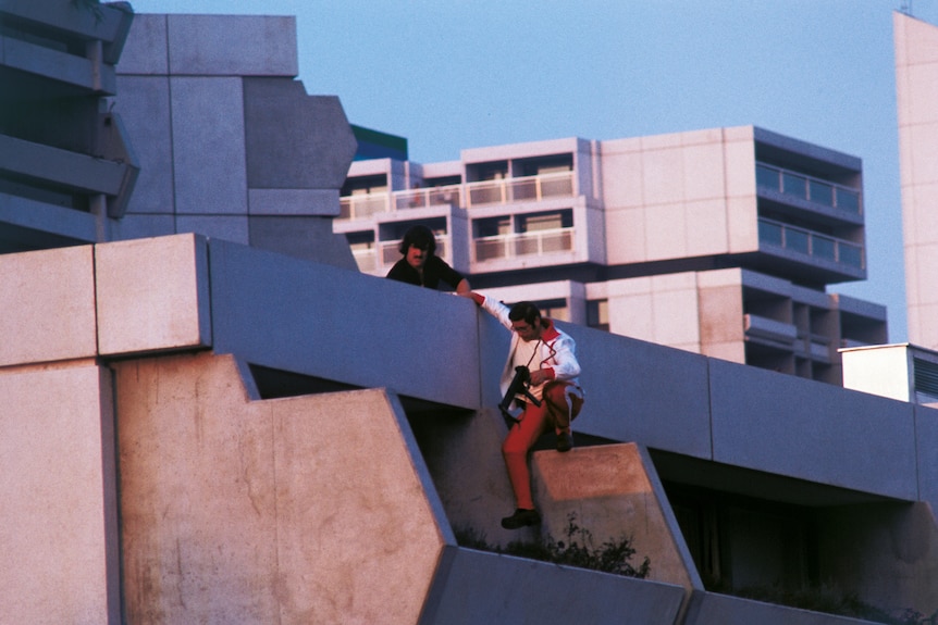 Armed police sit on a terrace above apartments holding guns.