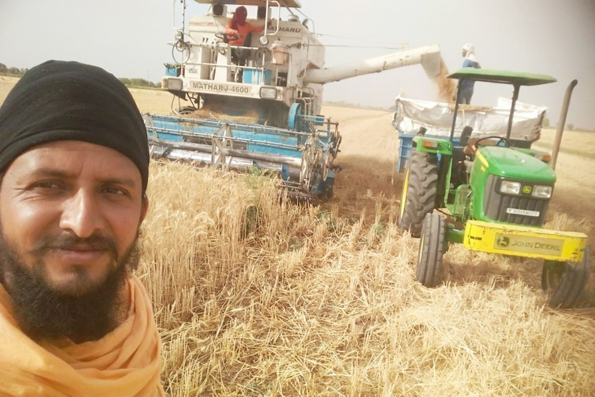 An Indian man in front a harvester in a wheat field.