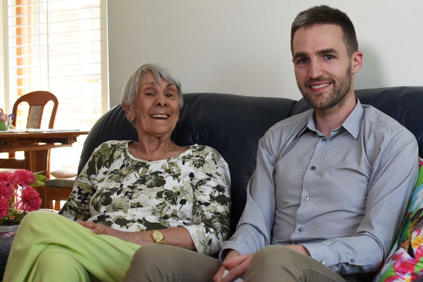 Adam and Margaret sit on the couch in Margaret's home.