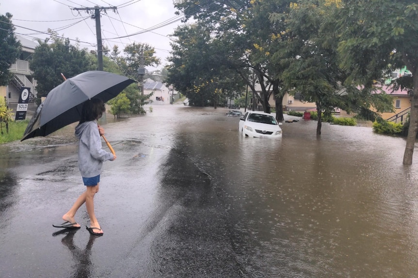 Someone holding an umbrella walking down a flooded road 