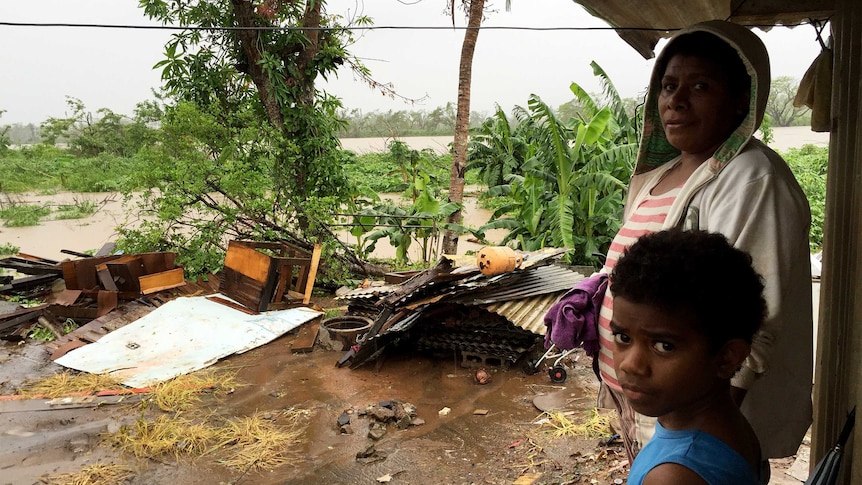 A Fijian family standing outside their home as floodwater reach their property.