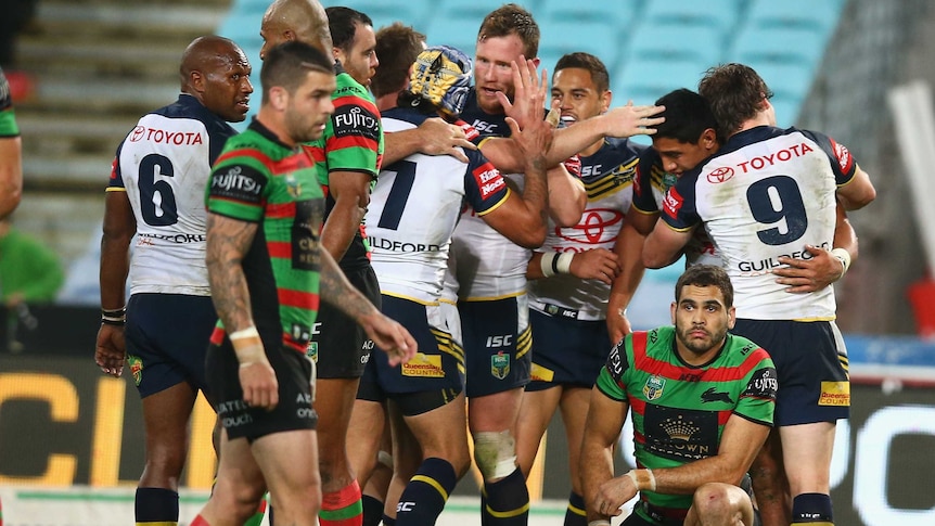 The Cowboys' Jason Taumalolo celebrates after scoring a try as Souths' Greg Inglis looks on.