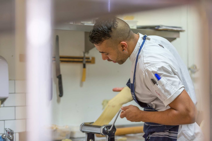 Ross puts a sheet of fresh pasta through a roller in the kitchen of a cafe.