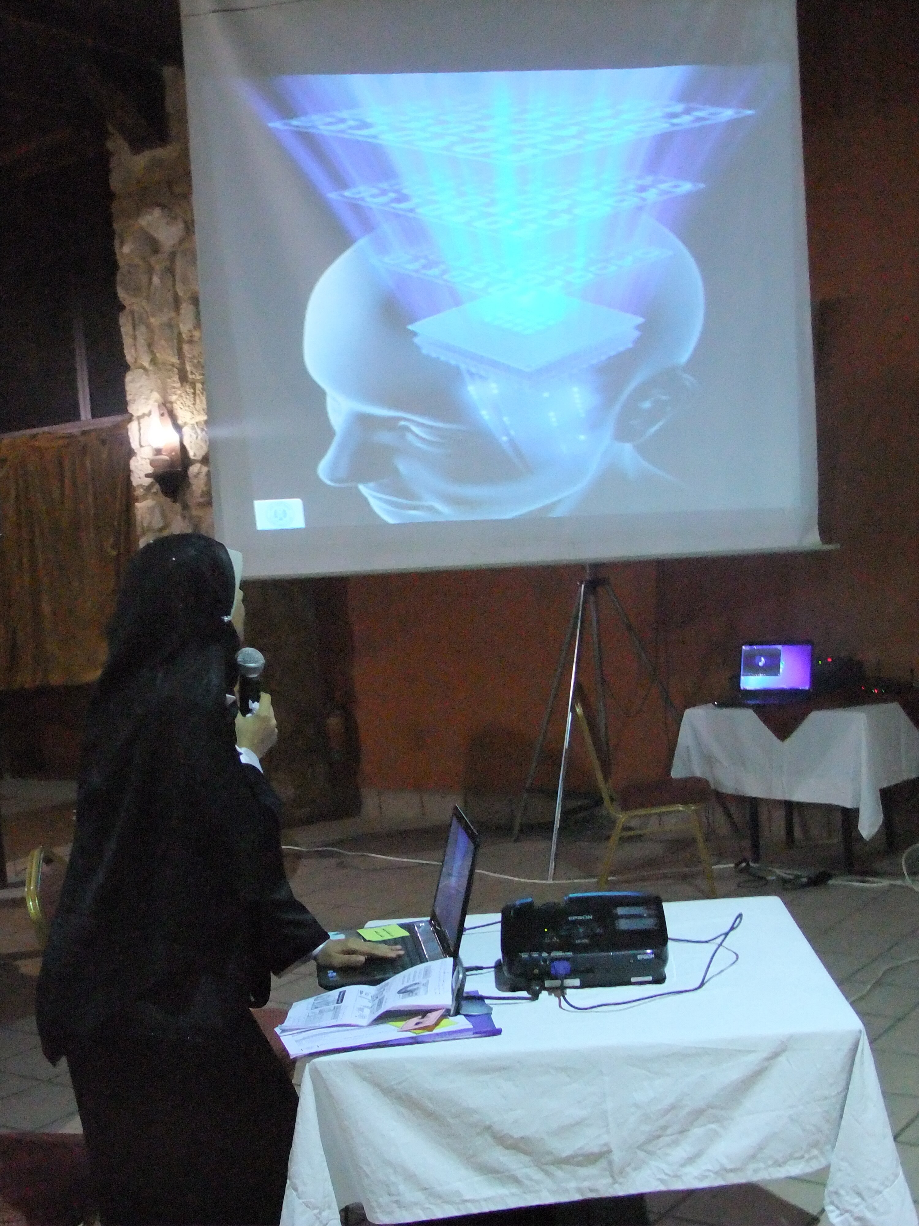A woman wearing a black head scarf faces away towards a projector. 