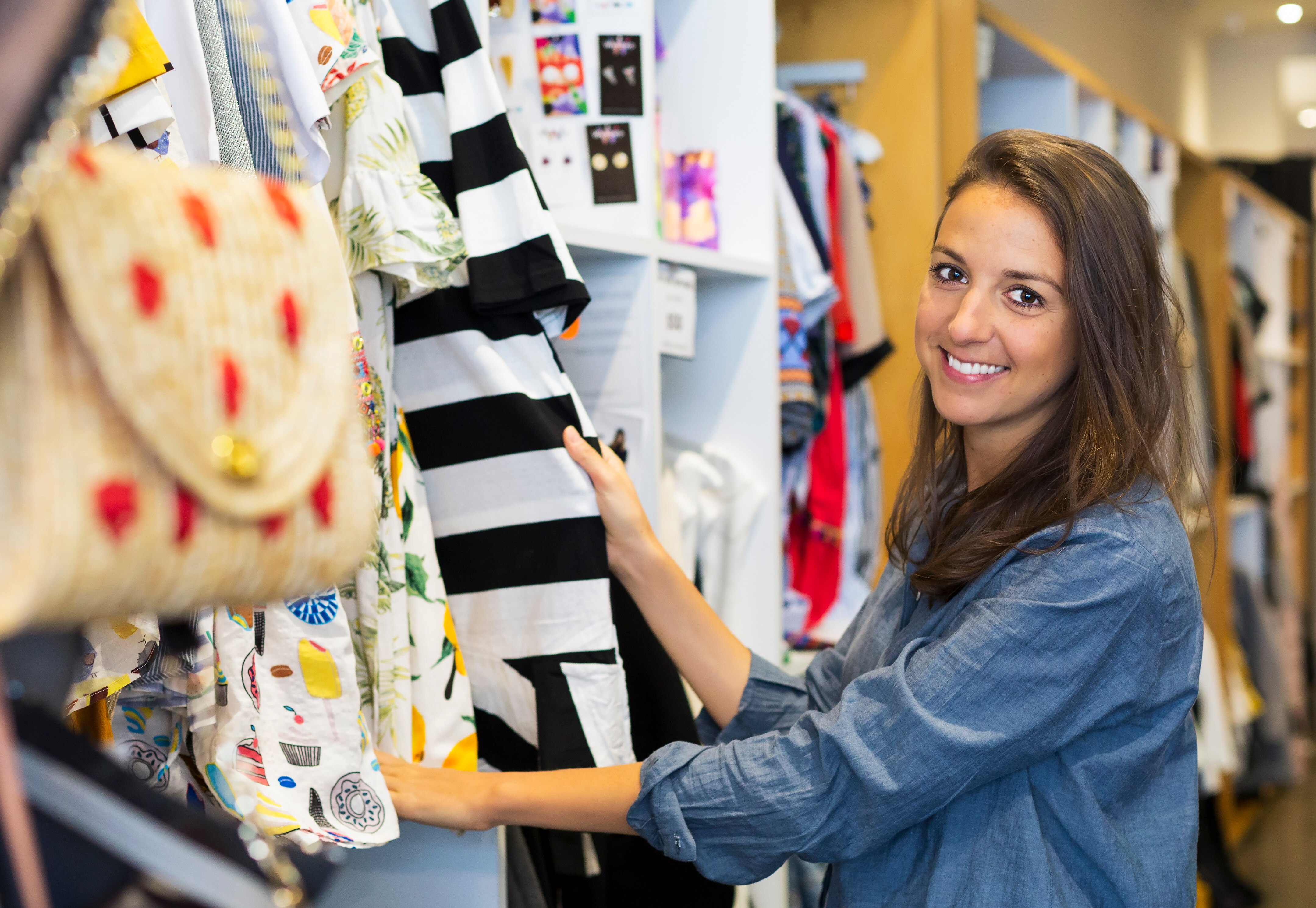 A woman holding an item of clothing, pulled from a clothing rack in a shop.