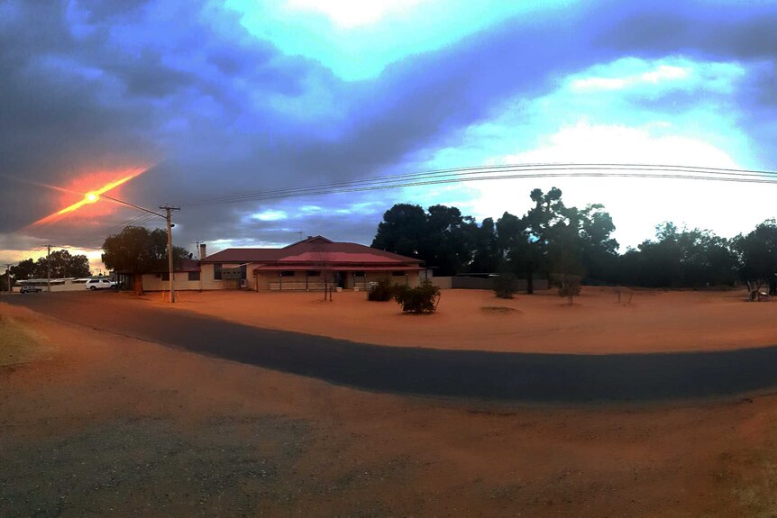 Wide shot street and house at sunrise with road snaking through red dusty landscape.