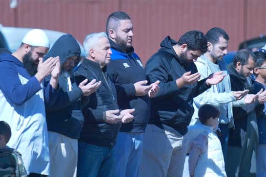 Men are praying in the Muslim faith by raising their hands.