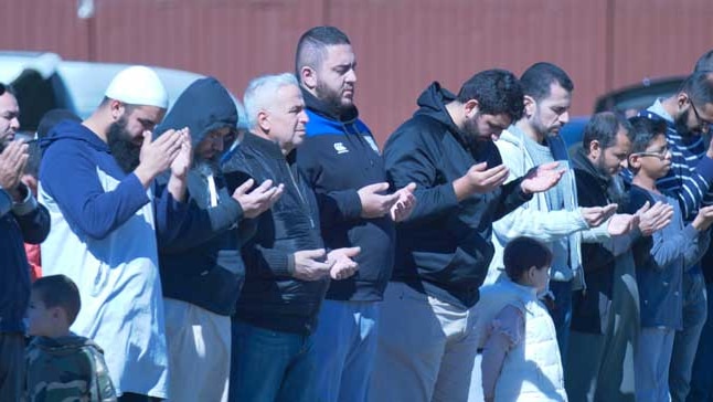 Men are praying in the Muslim faith by raising their hands.