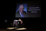 A coffin on a stage, draped in an Australian flag. An image of Tim Fischer 1946 - 2019 is on the big screen.