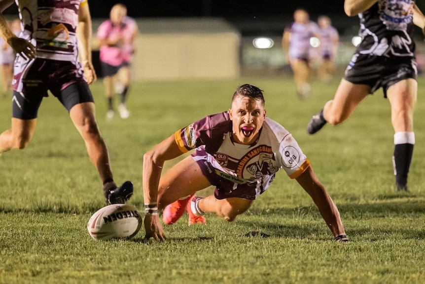 Rugby league player crawls on the ground in celebration after scoring a try. 
