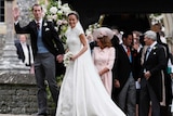 Pippa middleton wears a white high-neck lace gown and carries a white bouquet as her husband waves at photographers