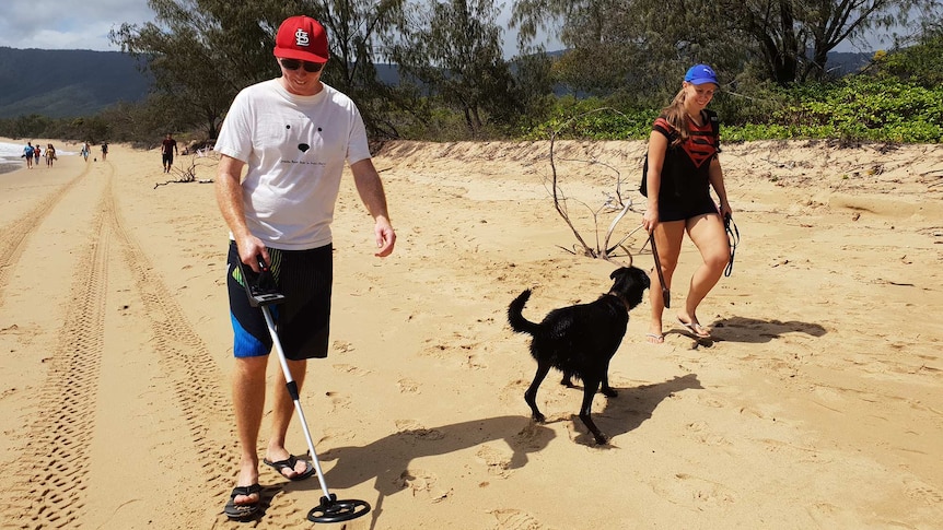 People walk with a metal detector and a dog on Wangetti Beach to search for clues in the murder of Toyah Cordingley.