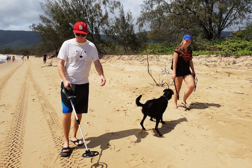 People walk with a metal detector and a dog on Wangetti Beach to search for clues in the murder of Toyah Cordingley.