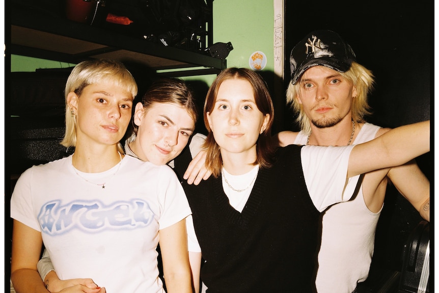 three women musos and a dude in a baseball cap with their arms around each other