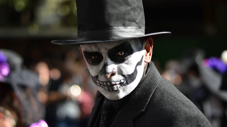 Man with a painted face wears black cloak and top hat