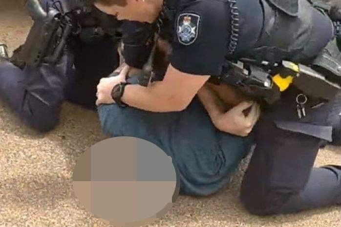 Two police officers arrest a man who is on the ground. His face is blurred.