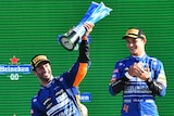 Racing drivers celebrate on the podium.