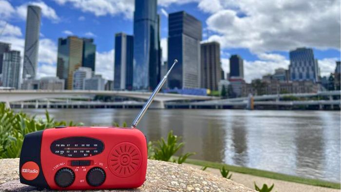 Red portable radio with an antenna in front of a city skyline by a river.
