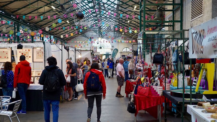 People walk past arts and cultural stands with goods inside an indoor market in Belfast