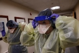 Two healthcare workers put on personal protective equipment