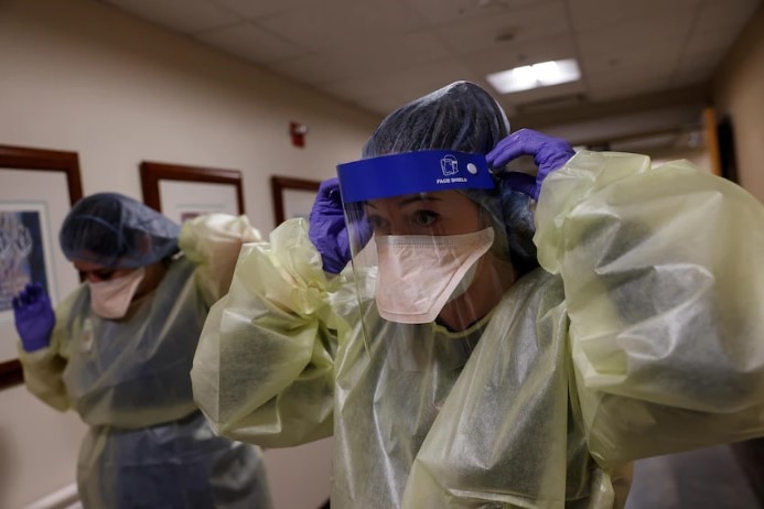 Two nurses in a corridor adjusting their protective gear.
