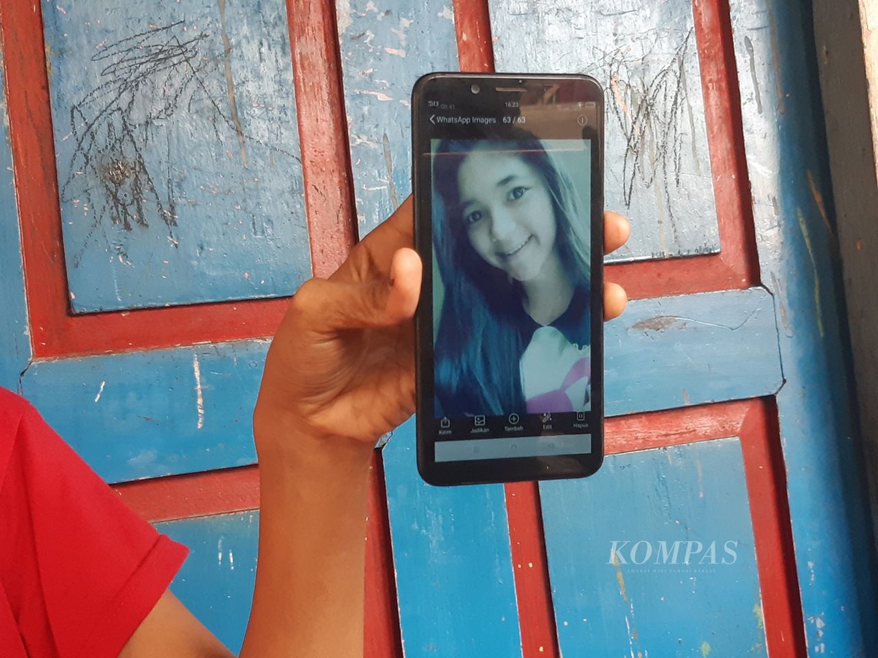 Medium close-up of a hand holding a cell phone with a photo of a woman with long hair on the screen.