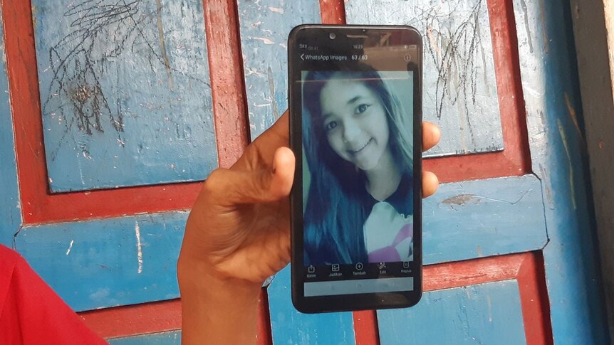 Medium close-up of a hand holding a cell phone with a photo of a woman with long hair on the screen.