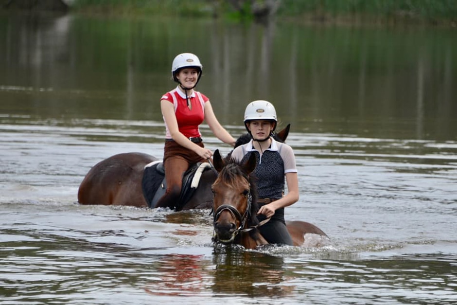 Two teenagers riding horses in a river
