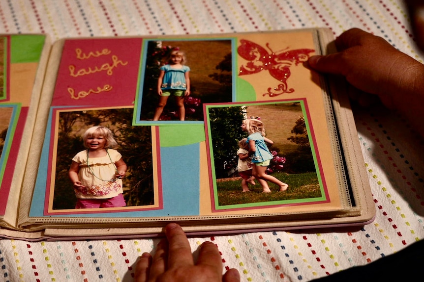 A photo album lies open on a kitchen table showing pictures of a young blonde girl