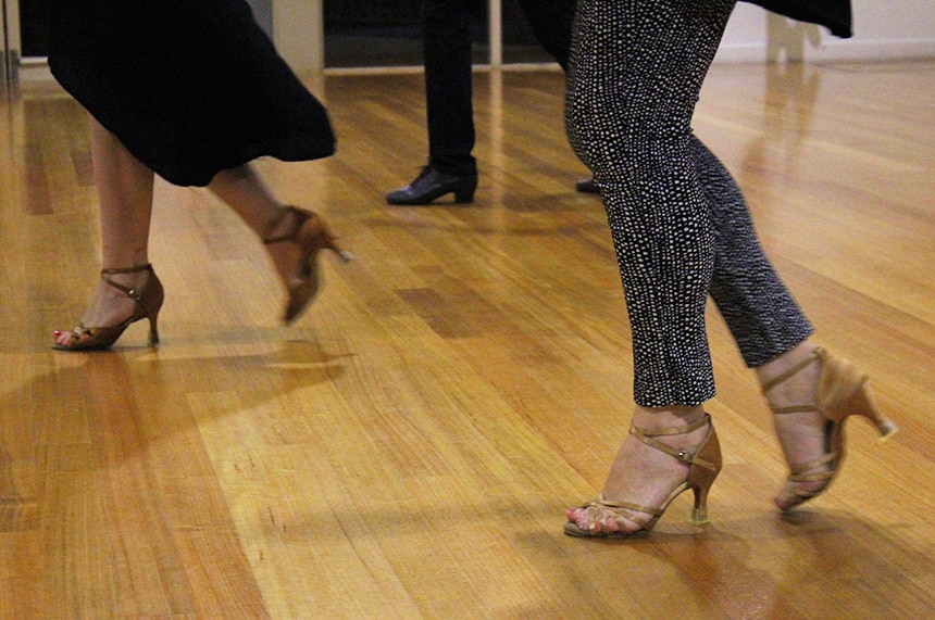 The feet of two women wearing dancing shoes on a hard wood floor.