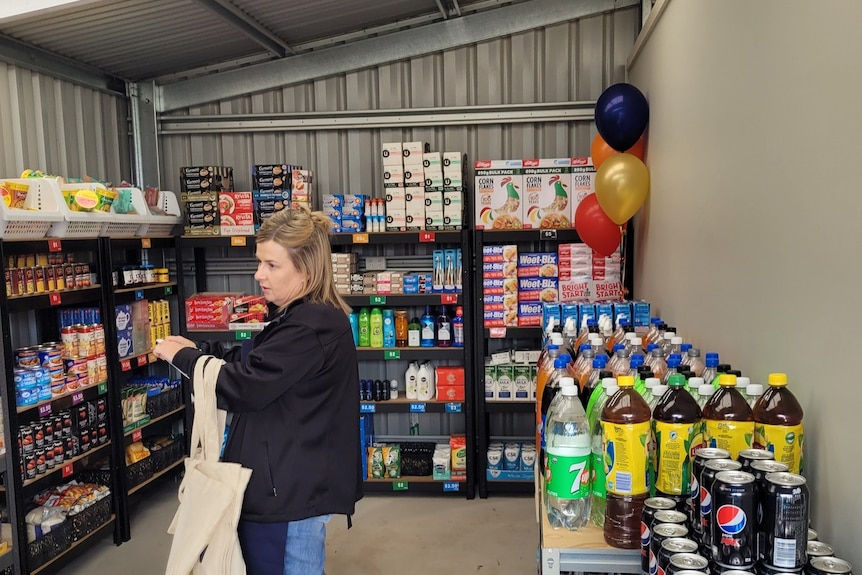 A woman shops inside a shed fitted with groceries on shelves