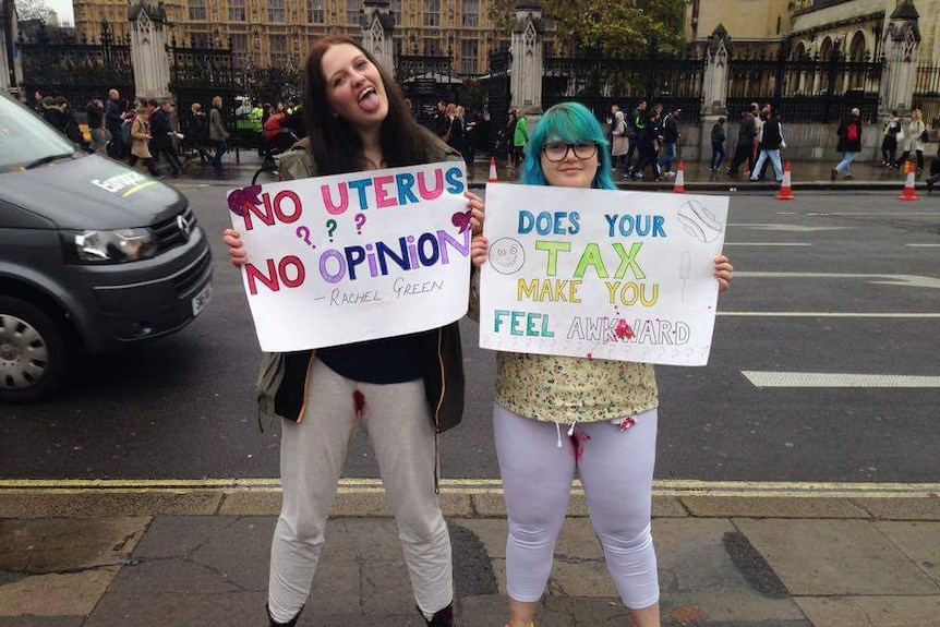 Charlie Edge and Ruth Howarth hold signs outside London's Parliament House to protest the Tampon Tax.