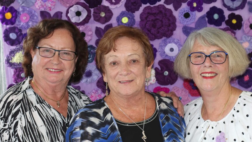 Evaline Bailey, Pauline Simpson and Judy Joukador stand in front of colourful purple fabric.