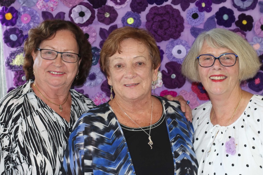Evaline Bailey, Pauline Simpson and Judy Joukador stand in front of colourful purple fabric.