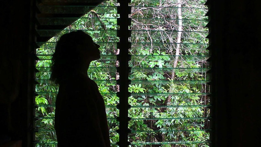 Silhouette of woman looking out window with green garden outside.