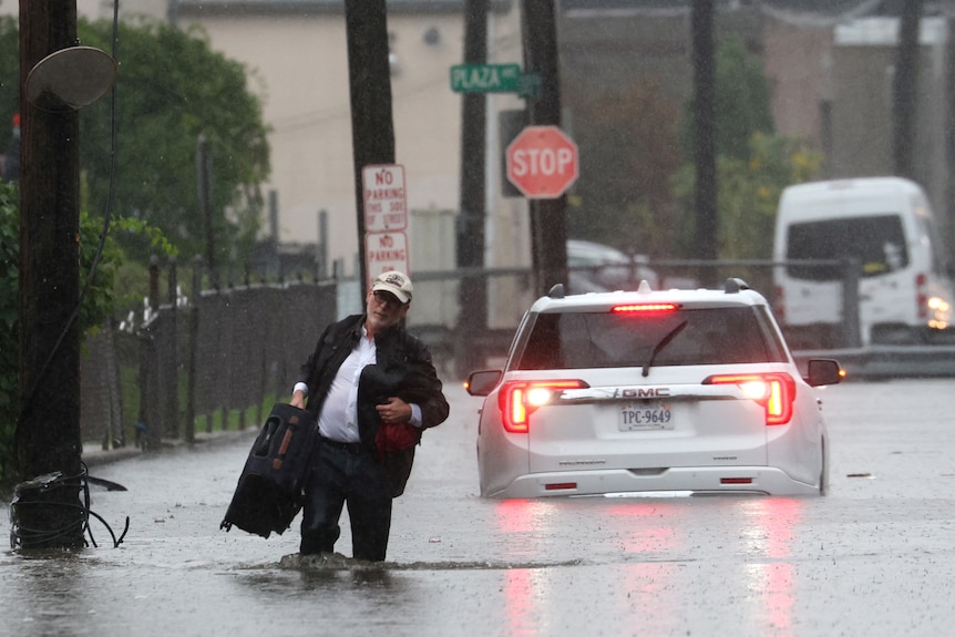 .A man carries his belongings as he abandons his vehicle in flood.