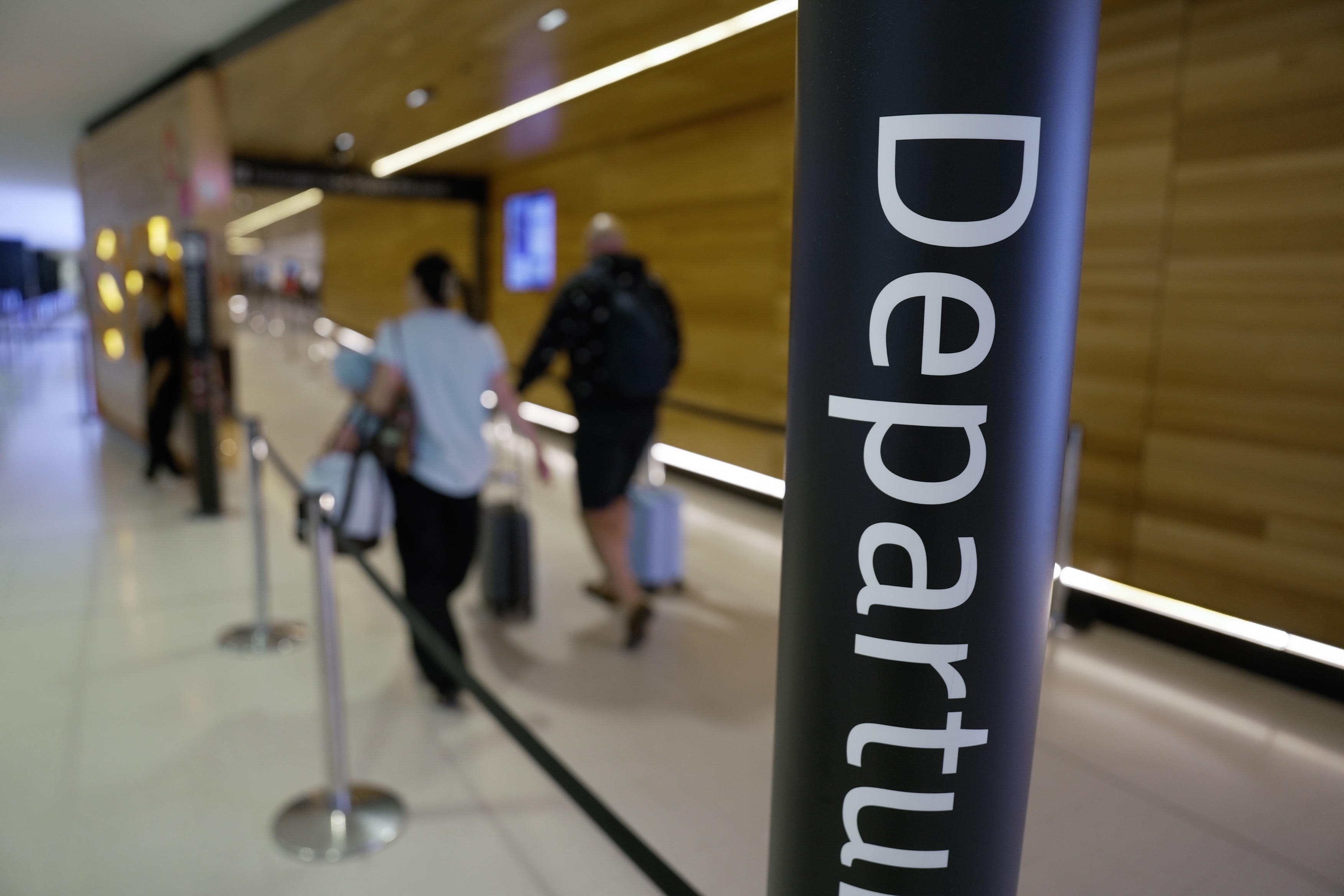 People walking into a gate at an airport with a Departures sign in the foreground.