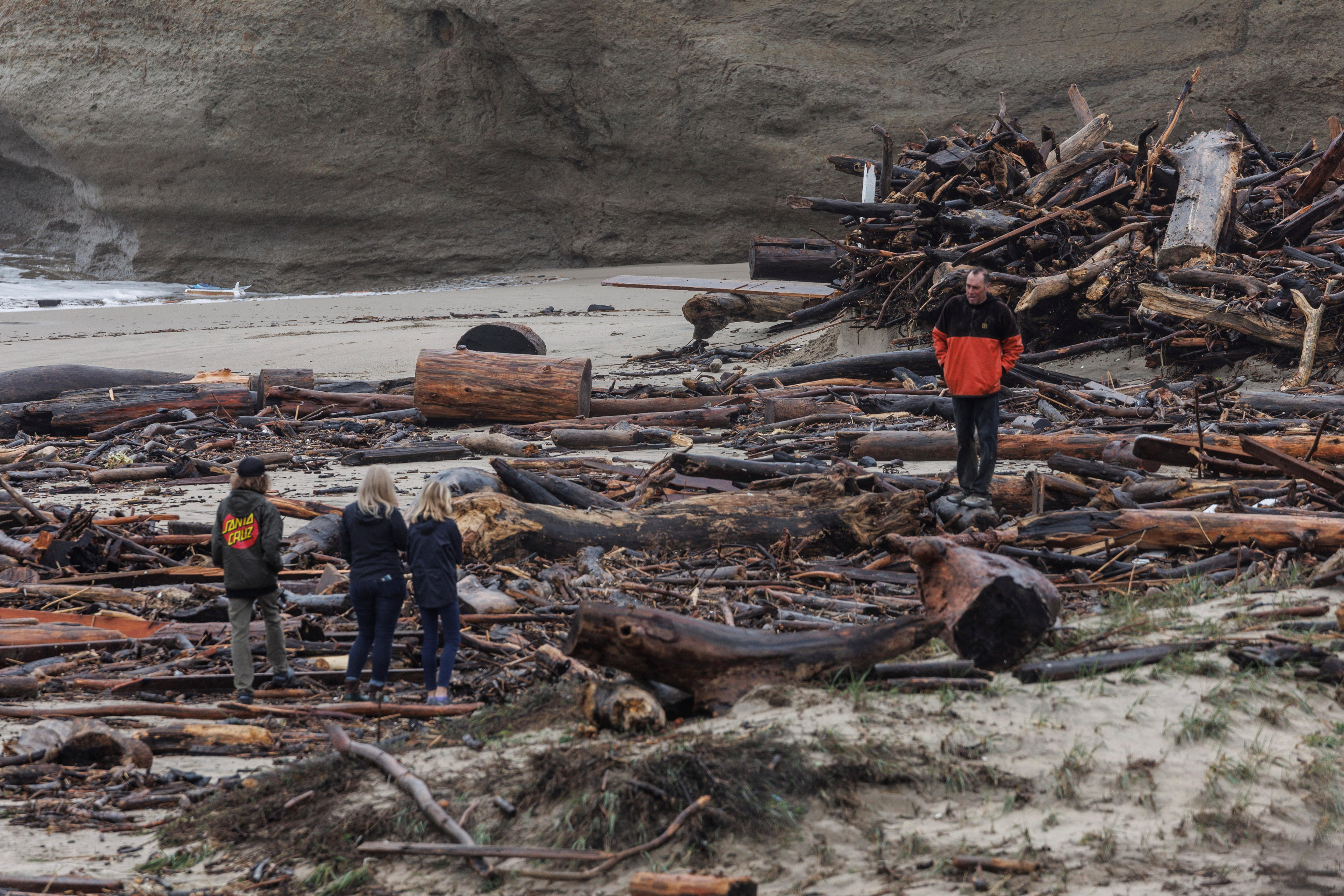 当地居民在加利福尼亚州圣克鲁斯的暴风雨过后看着海滩上的碎片。