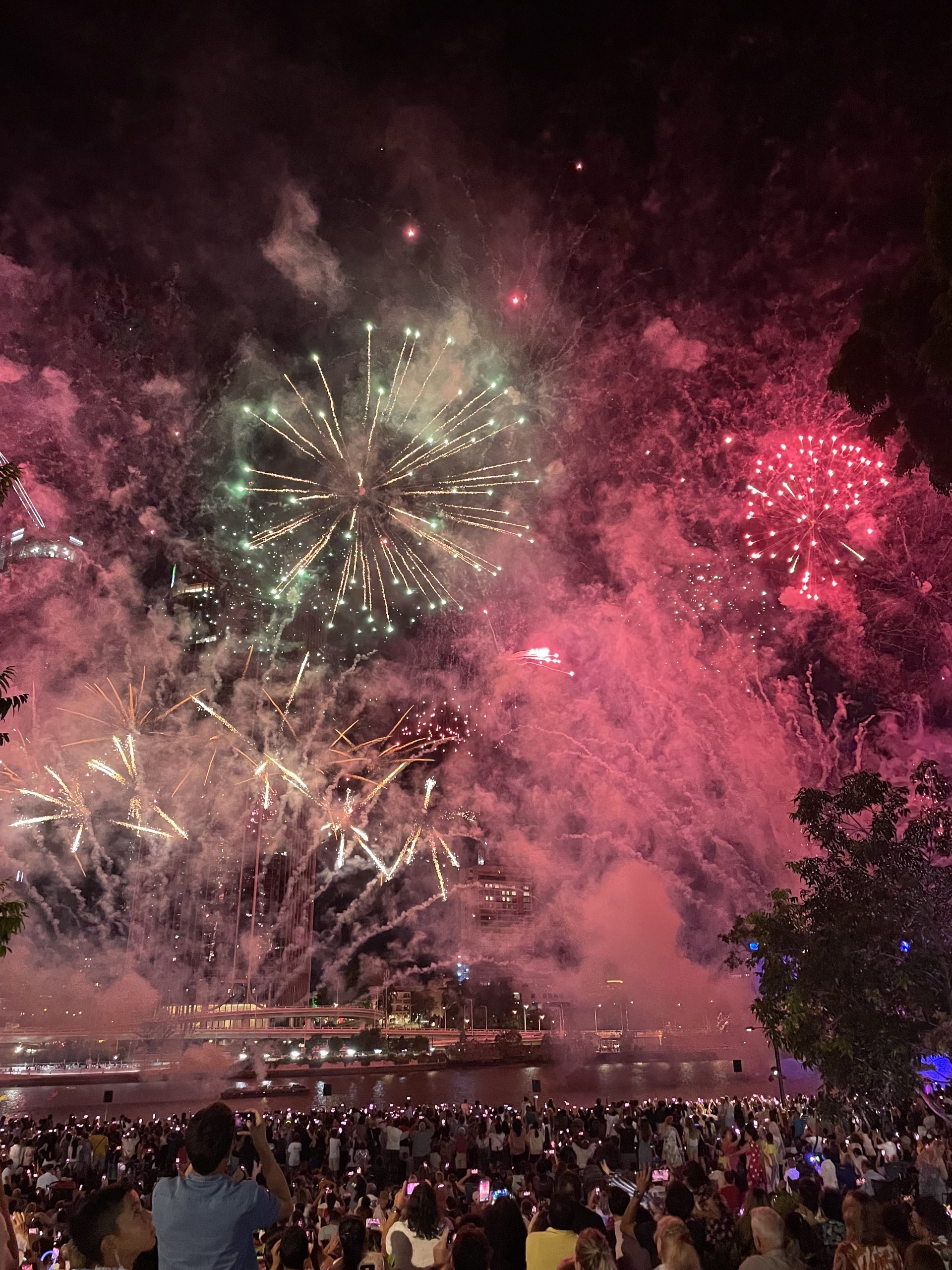 Una imagen amplia de una multitud mirando los fuegos artificiales en el cielo nocturno sobre el río Brisbane.