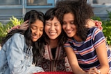 Three teenage girls sit and hug at a red table outside