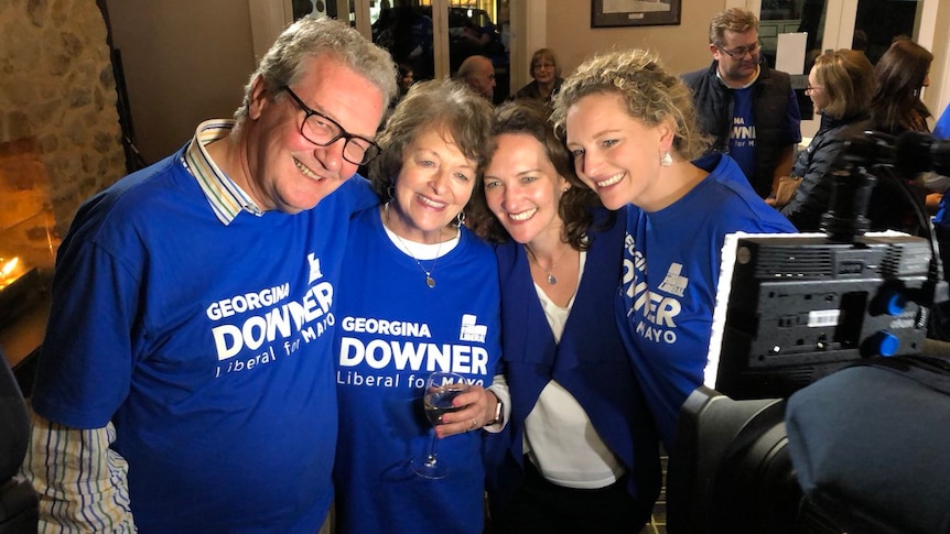 The Downer family in matching blue shirts smile at a video camera.