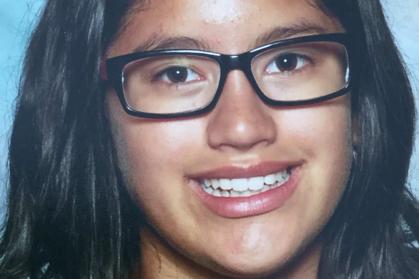 A girl with dark hair and glasses smiles at the camera.