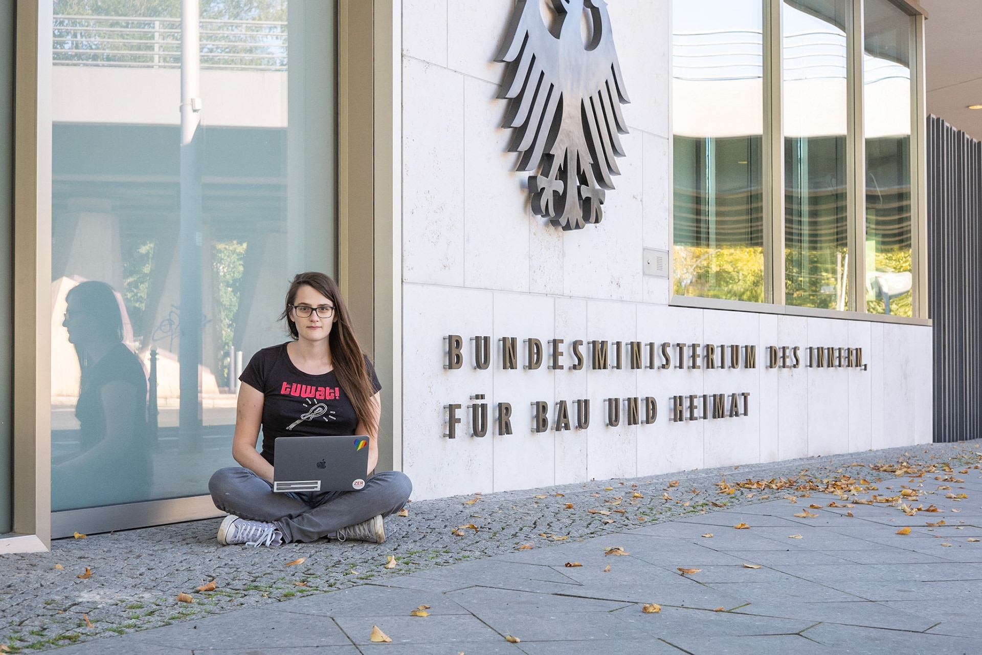 A young woman sits on the ground with a laptop outside a public building in Germany