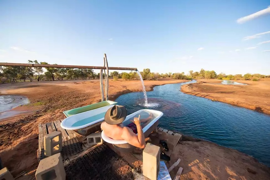  A tourist sits in a bathtub overlooking a stream surrounded by red dirt.