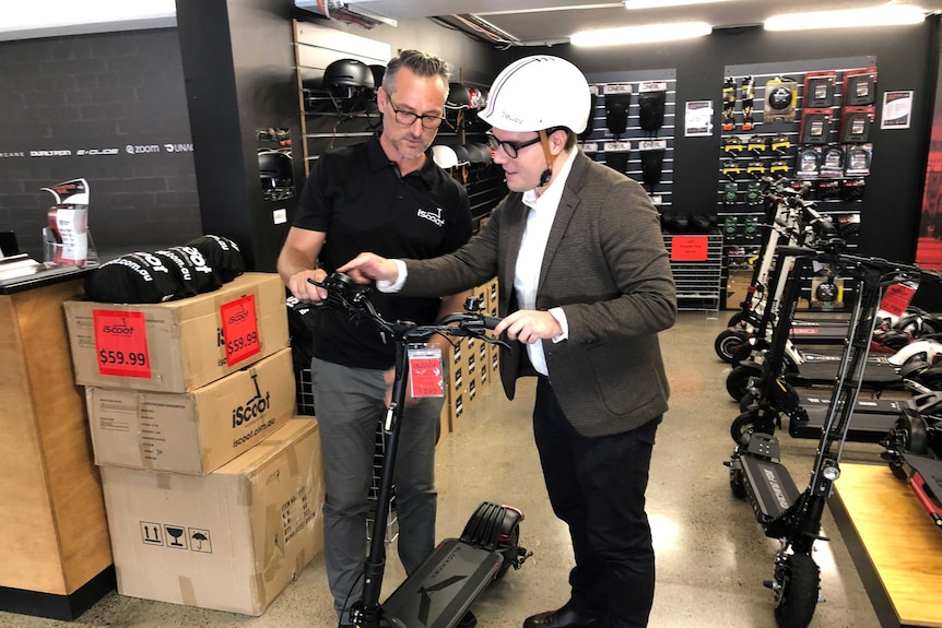 Two men stand with an e-scooter looking at the device in an e-scooter shop.