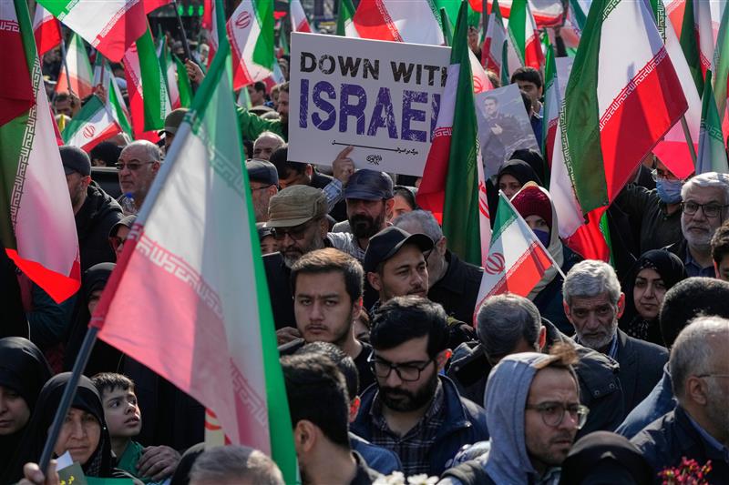 A crowd of people hold Iran flags. One holds a sign that says Down with Israel