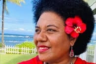 A Fijian woman wearing a red dress and hibiscus flower in her ear outside 